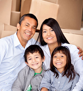 Family with smiling children sitting in front of moving boxes.